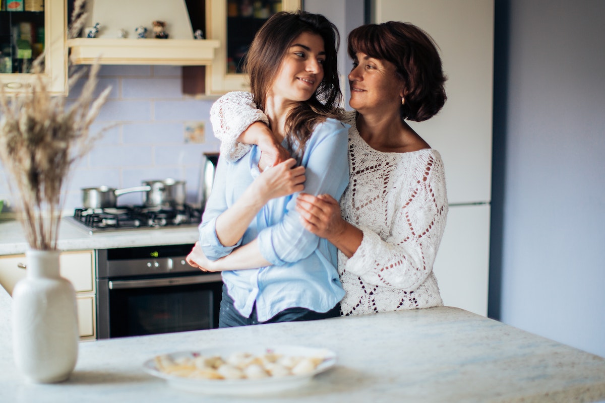 A mother and daughter hugging in a kitchen.