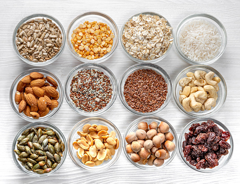 Seeds, nuts, grains in glass bowls on a white wooden background.