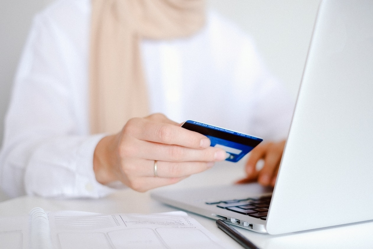 A seated woman with a laptop in front of her holds a credit card.