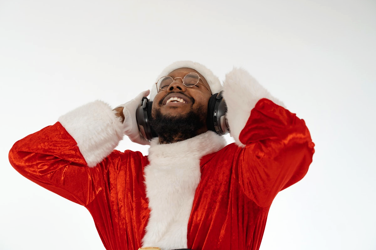 A smiling man in a Santa costume wears over-ear headphones.