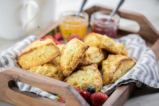 A pile of scones and jams on a wooden tray.