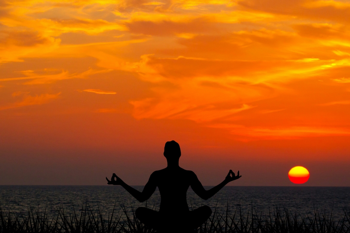 Person meditating in front of a sunset
