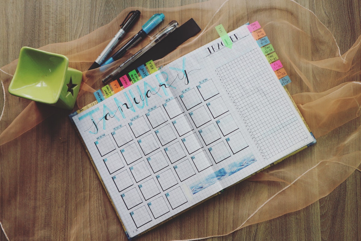 A bullet journal lays open on a table with with a January calendar spread. Several writing instruments are strewn around it.