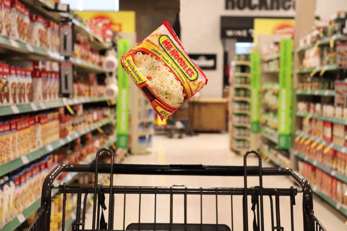 Package of Mr Noodles falling into a shopping cart