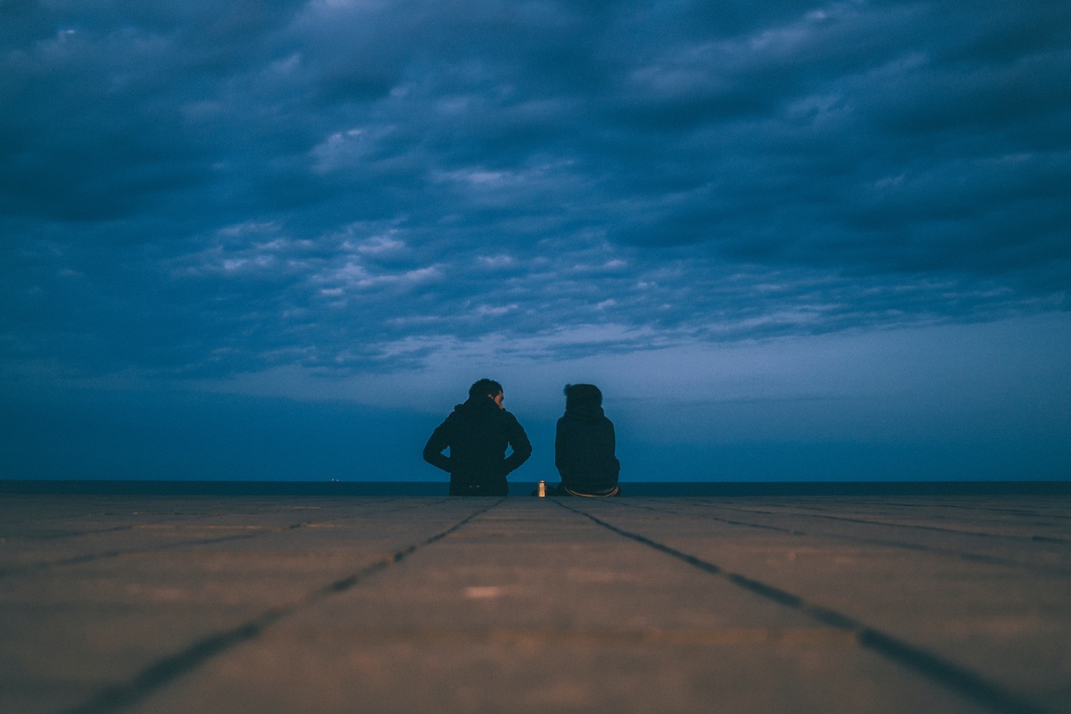Couple sitting at the edge of a dock at dusk