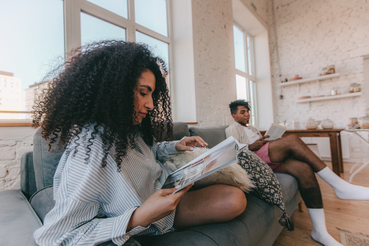 Woman sitting on sofa reading a magazine beside man with a book