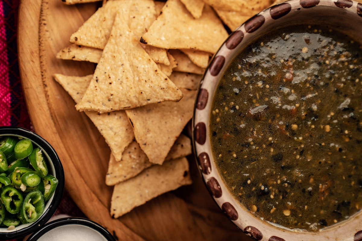 A bowl of black bean salsa next to tortilla chips and sliced jalapeno peppers