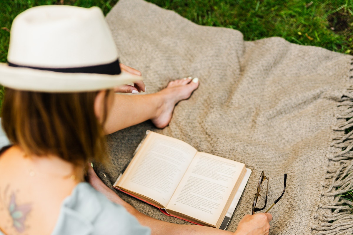 Woman sitting on a blanket on the grass with bare feet and reading a book