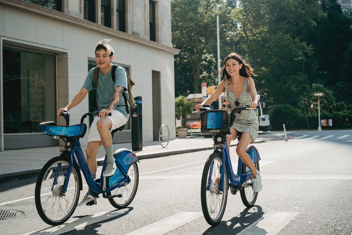 Two young adults riding bicycles along a city street in summer.