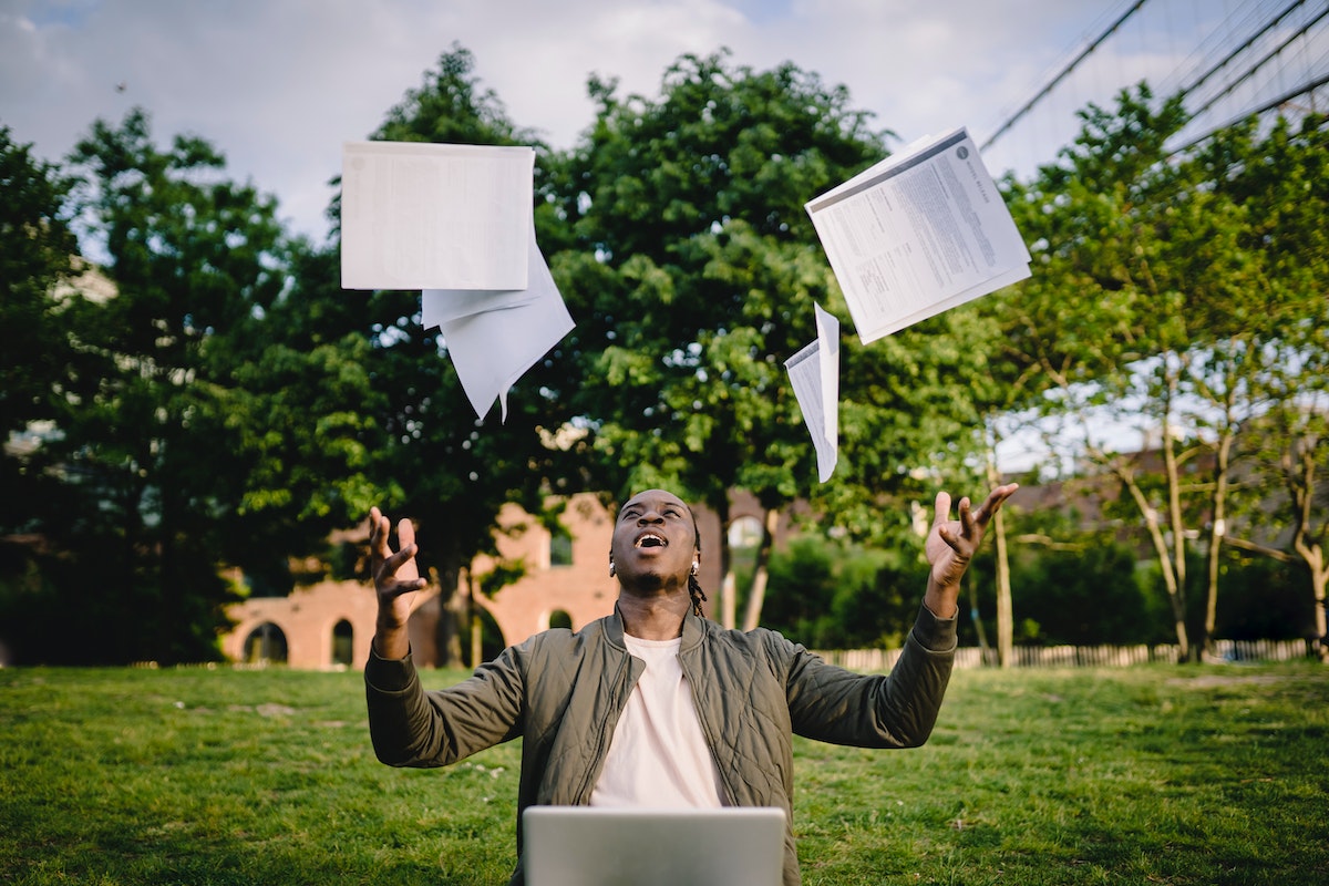 Person standing outside in front of a laptop throwing papers in the air