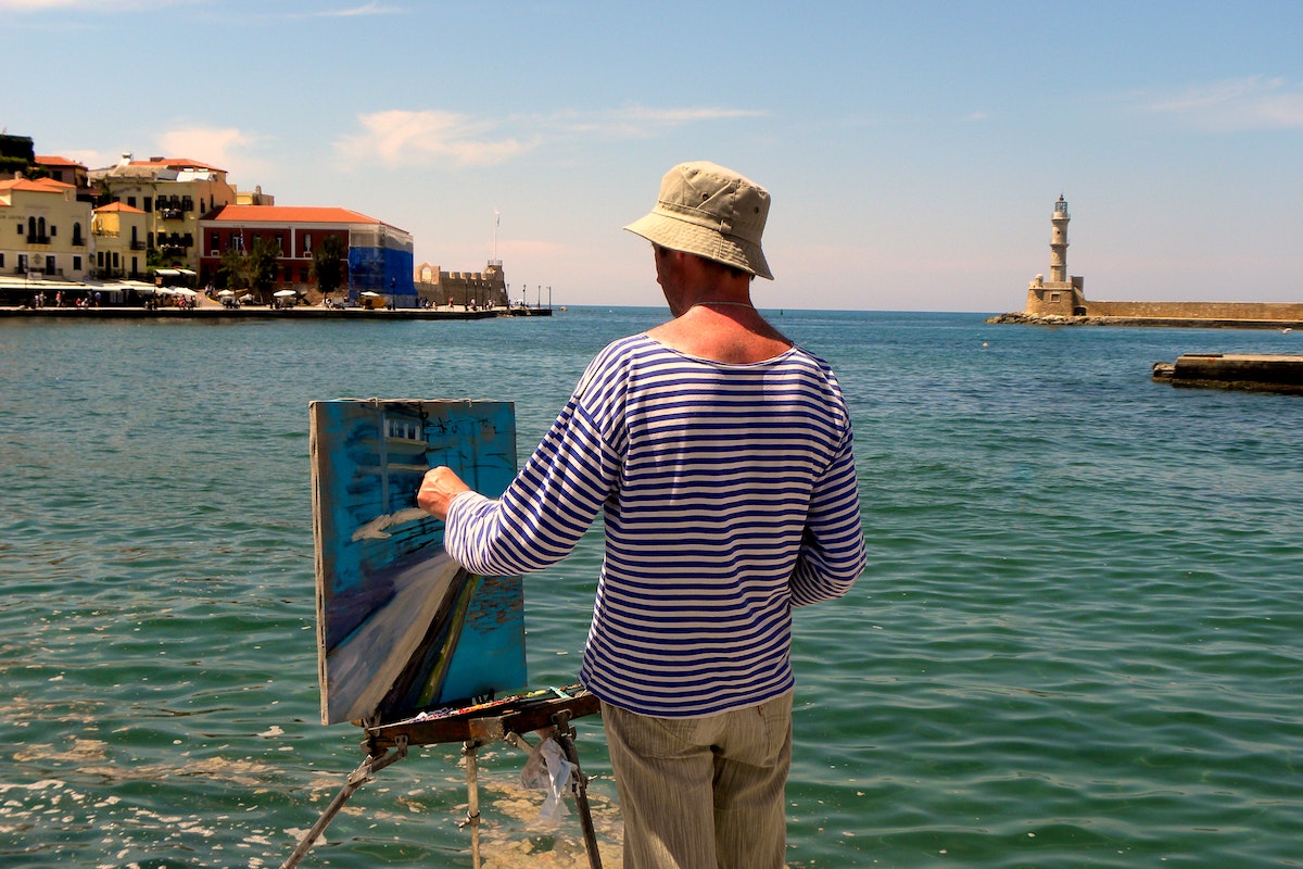 Person painting a picture while standing beside the ocean.