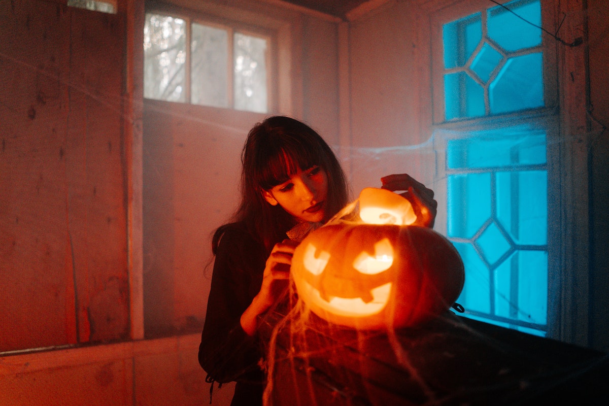 Woman beside a jack-o-lantern in a dark room with cobwebs