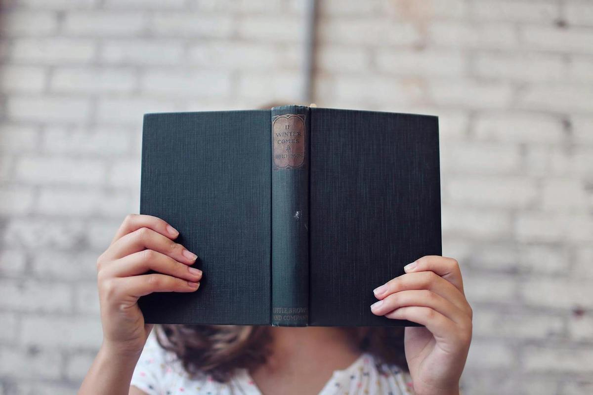 A girl holds an open, old-looking book in front of her face.