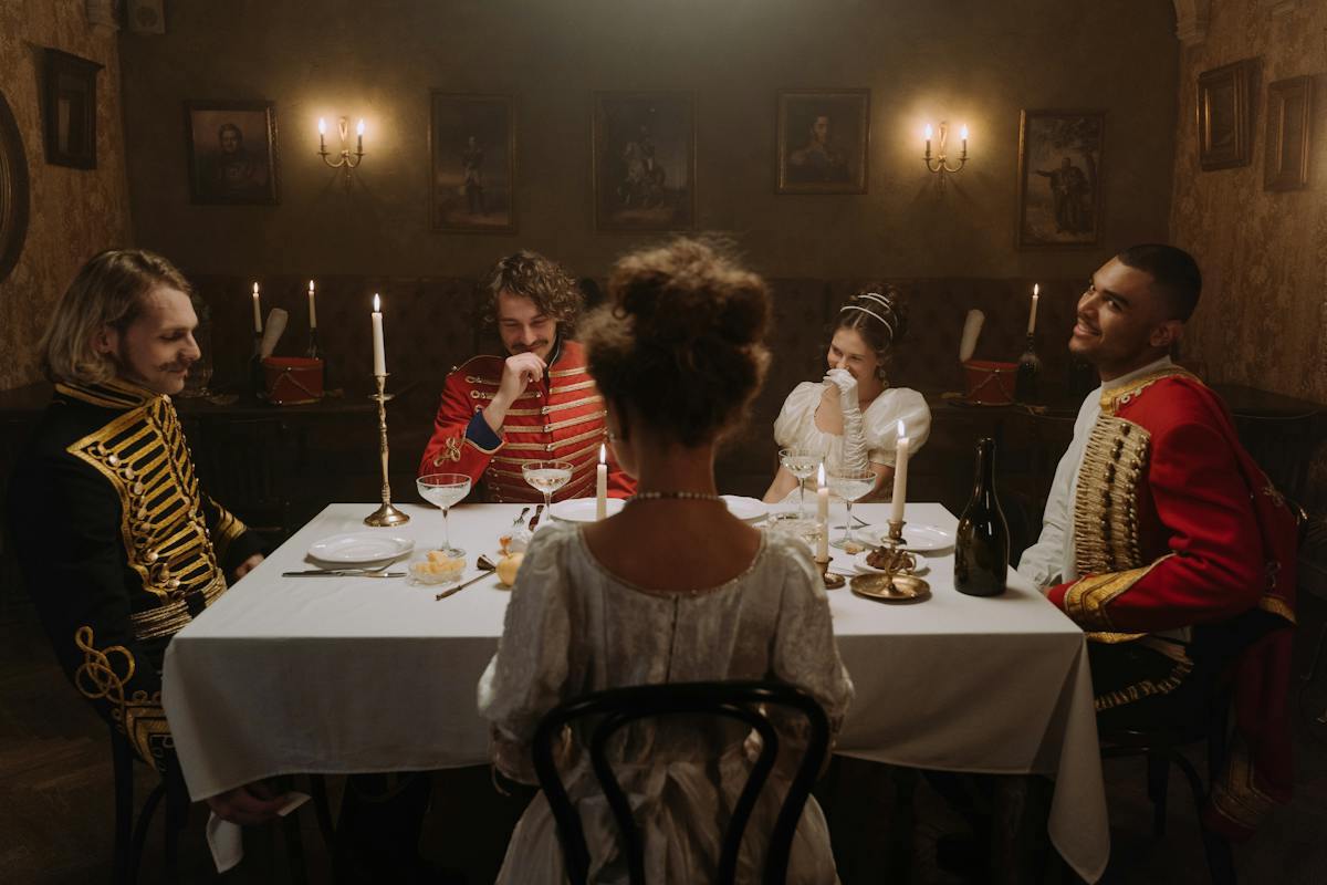 5 young adults sitting around a dinner table while wearing replica 18th-century clothes
