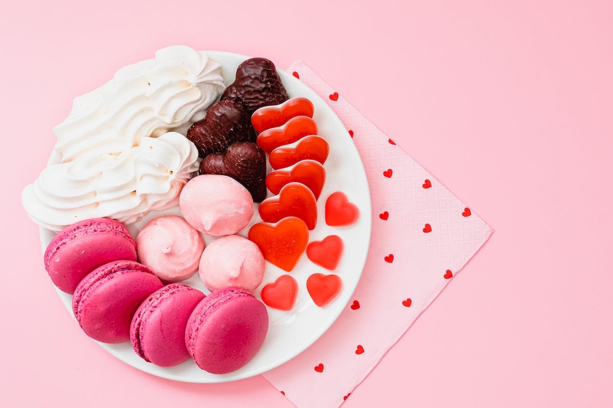 Red, white, pink, and chocolate sweets on a white plate, sitting on a napkin with pink hearts