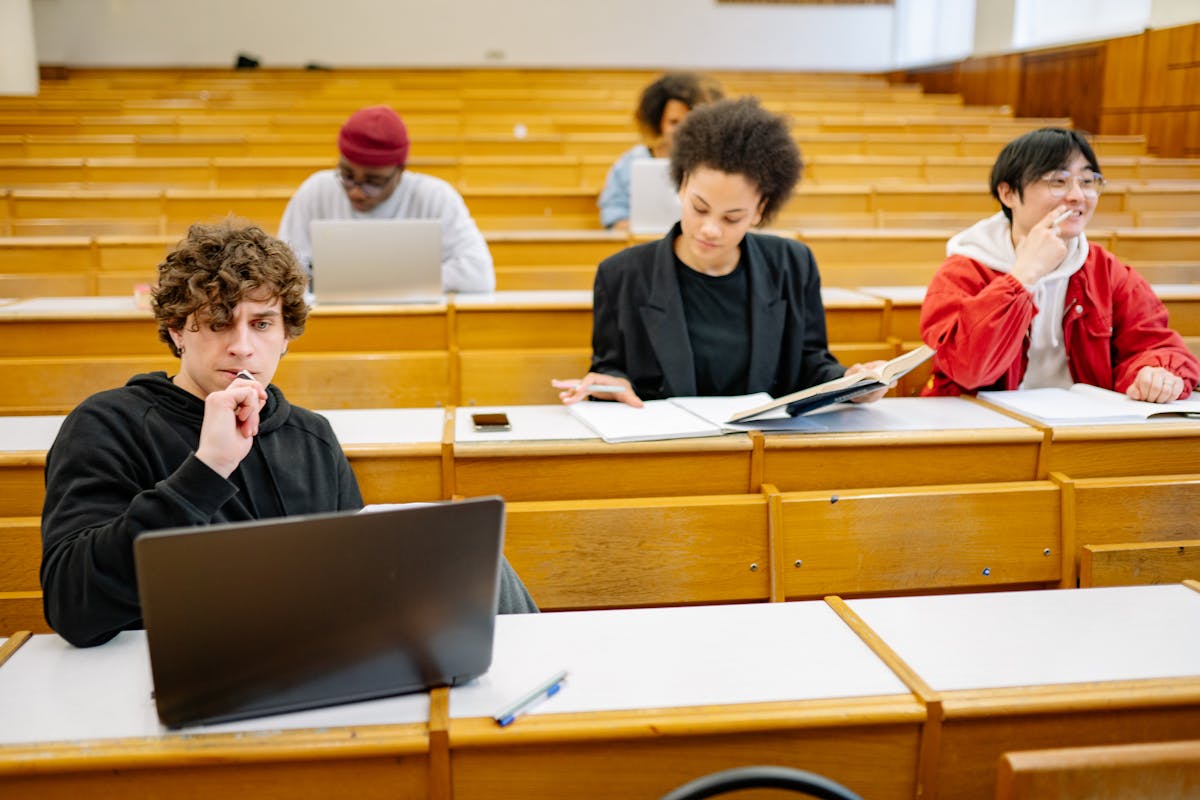 Students sitting in a lecture hall taking notes on computer and paper