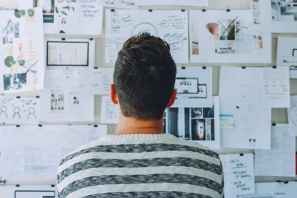 A photo from behind of a student looking at a bulletin board covered in pieces of paper with various pictures and writing on them.