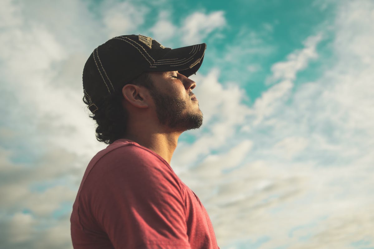 Young man wearing a ball cap staring at the sky with his eyes closed
