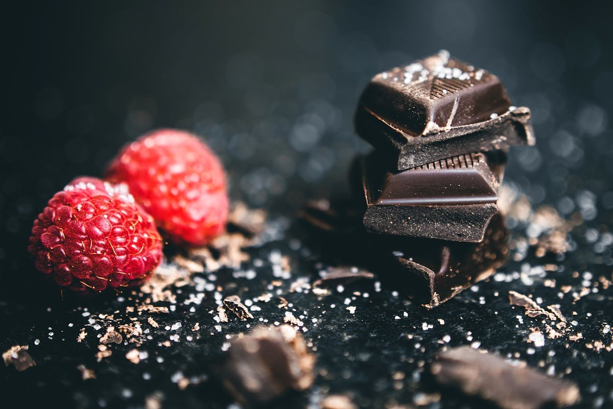 Two raspberries sitting beside a pile of dark chocolate