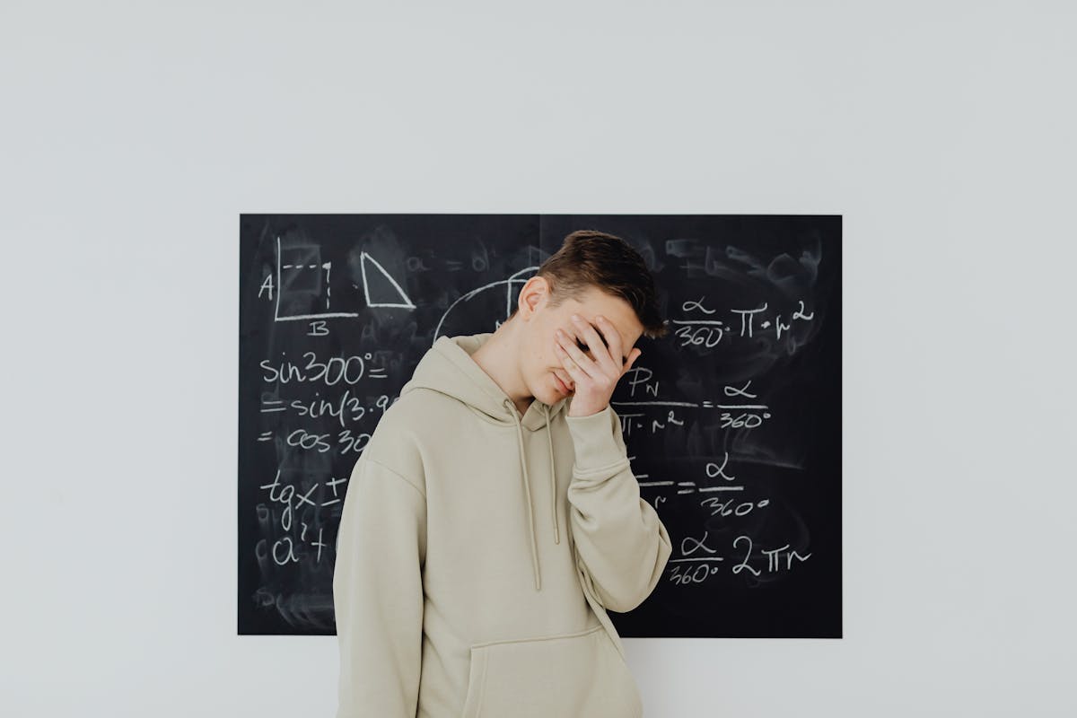 Student holding their head in their hand, standing in front of math equations written on a chalkboard