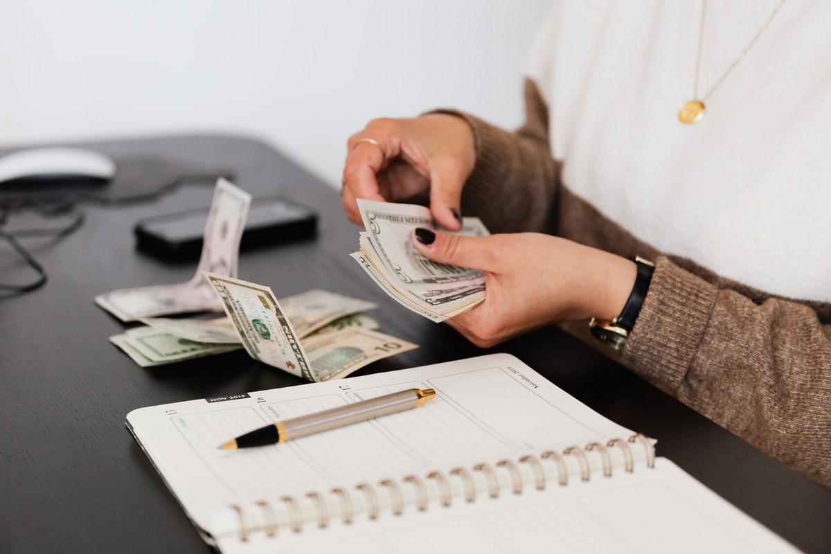 A girl counts dollar bills above a planner.