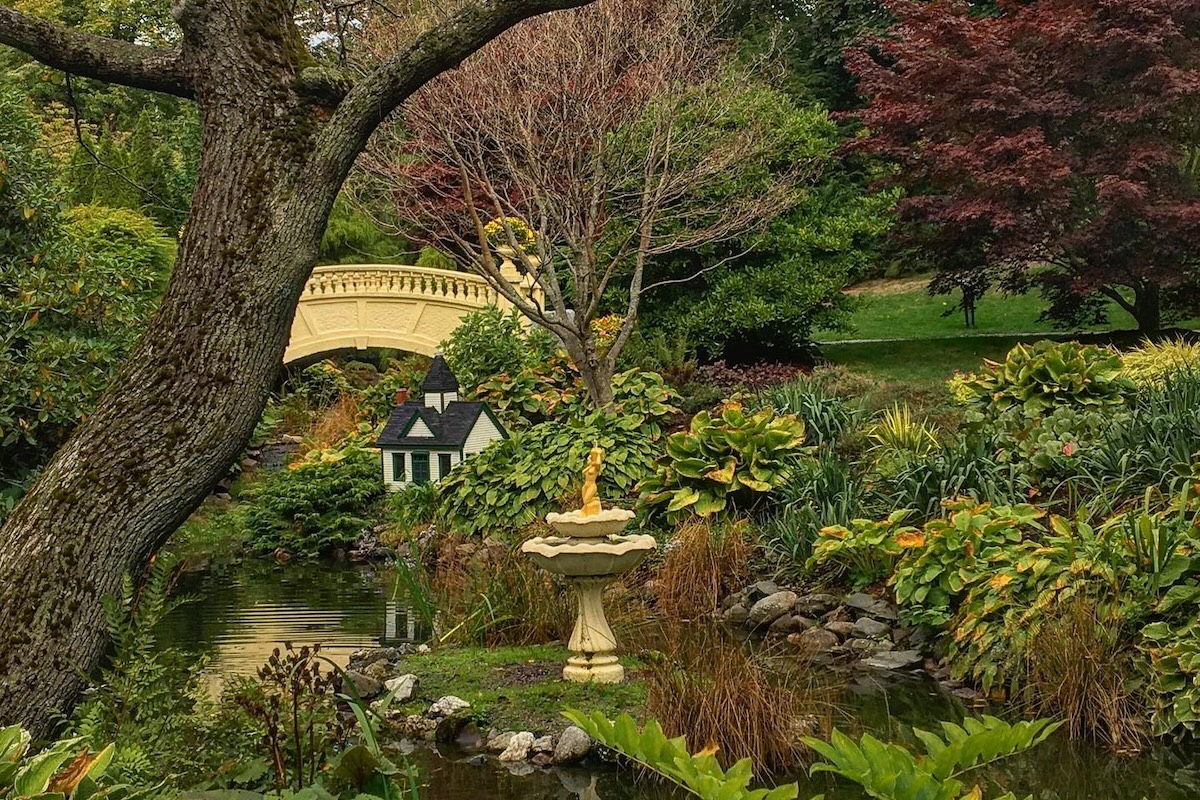 A bridge going over a small stream surrounded by trees, plants, and flowers