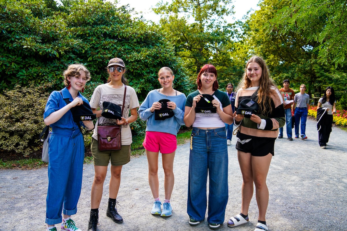Five students stand outdoors while holding black beanie hats with the Dal logo on them.