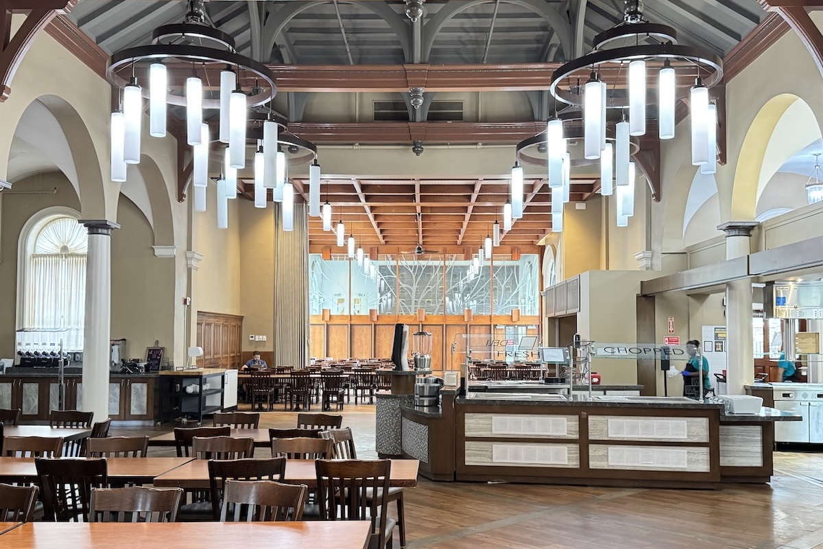 Food stations and tables and chairs in a room with a large vaulted ceiling and modern chandeliers hanging.